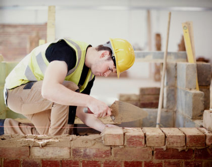 A student at Sunderland College, wearing a hi-vis jacket and hardhat, and working on bricklaying