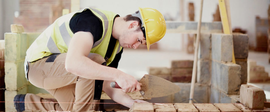 A student at Sunderland College, wearing a hi-vis jacket and hardhat, and working on bricklaying