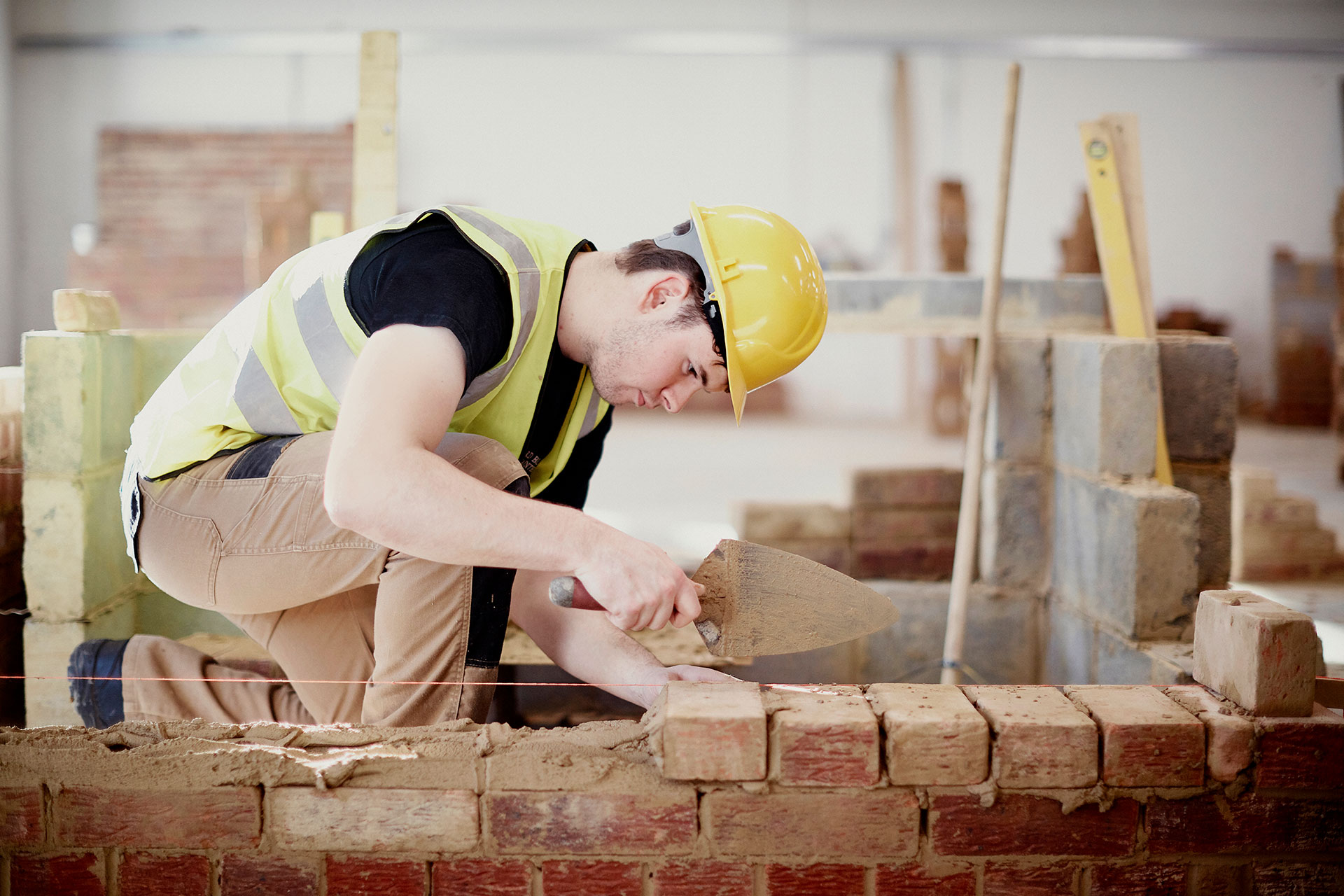 A student at Sunderland College, wearing a hi-vis jacket and hardhat, and working on bricklaying