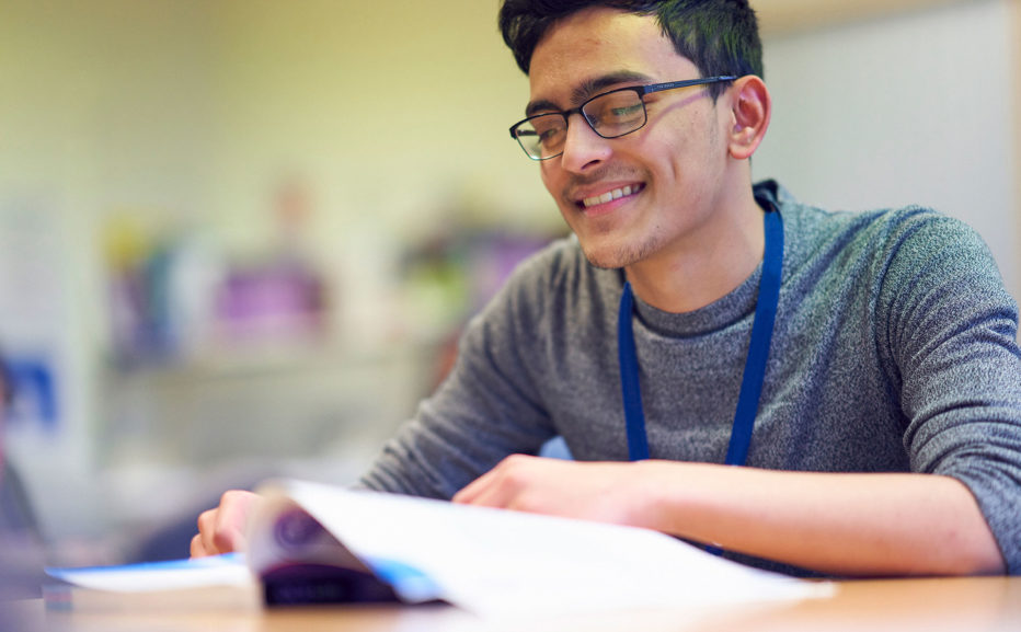 A student at Sunderland College, smiling and reading a textbook