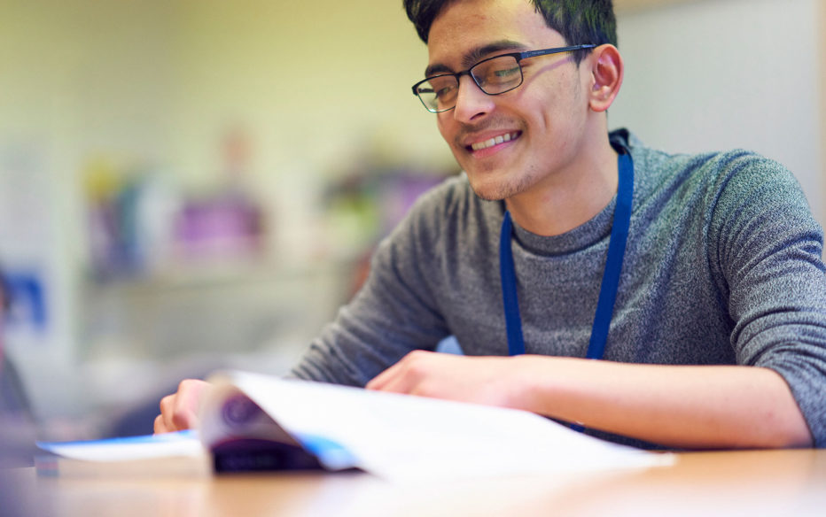 A student at Sunderland College, smiling and reading a textbook