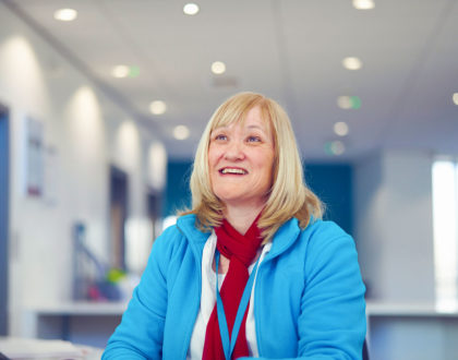 Female receptionist at Sunderland College sits at desk, smiling at camera.