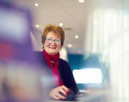 Female receptionist at Sunderland College sits at desk, smiling at camera.