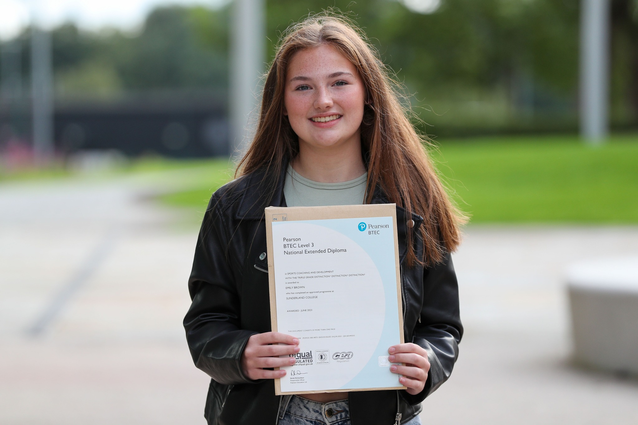 Emily Brown smiles at the camera while holding her college certificates.