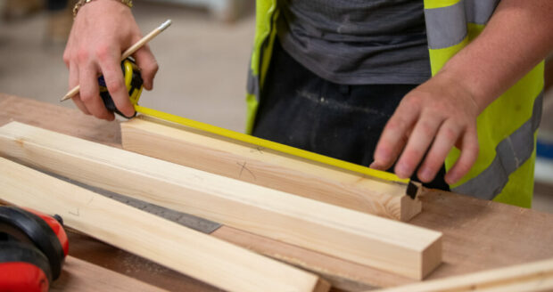 An image of a student at Northumberland College Ashington Campus, measuring a plank of wood with a tape measure